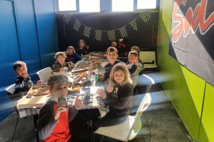Eight children sitting at a table having a party with food and drinks.