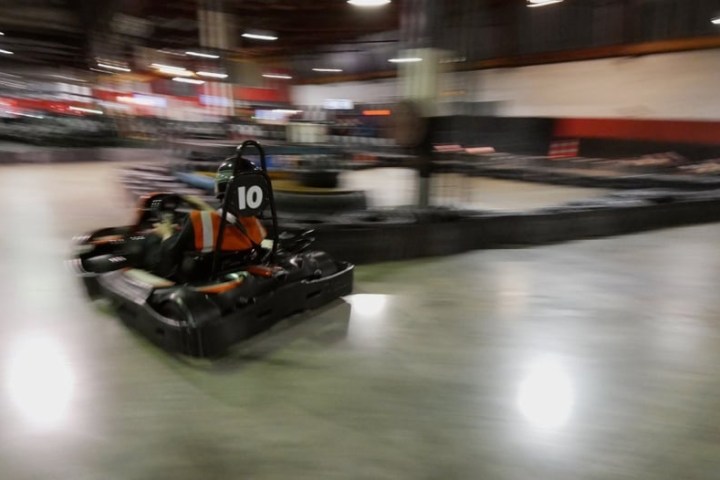 Person driving a go-kart indoors on a track, motion blur indicates speed.