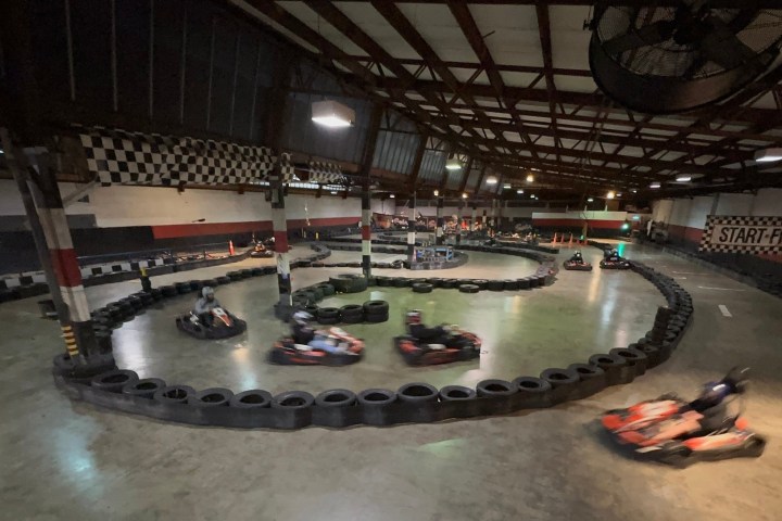 Indoor go-kart track with racers speeding around the course.