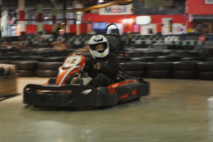 Person in helmet driving a go-kart indoors on a track.