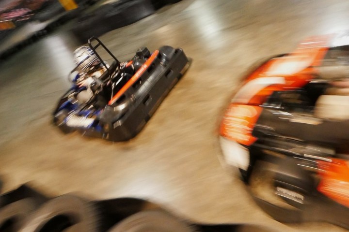 Two go-karts racing indoors on a track, captured in motion blur.