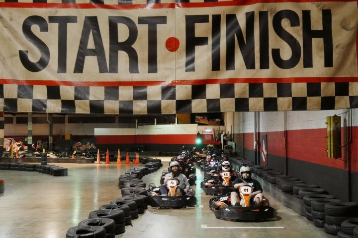 Indoor go-kart racers at the starting line under a 'Start-Finish' banner.